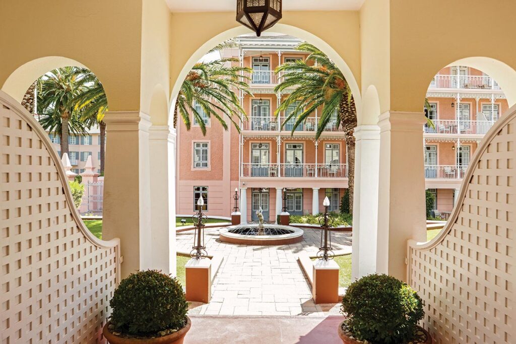 An archway leads to the hotel’s fountains, statues, and gardens filled with pink flowers in a part of the hotel called Hof Villa.