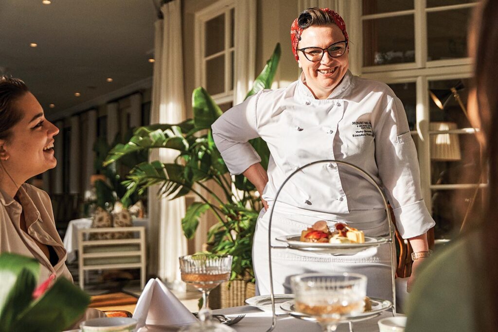 Award-winning pastry chef Vicky Gurovich stands beside a two-tiered tea server packed with pastries.