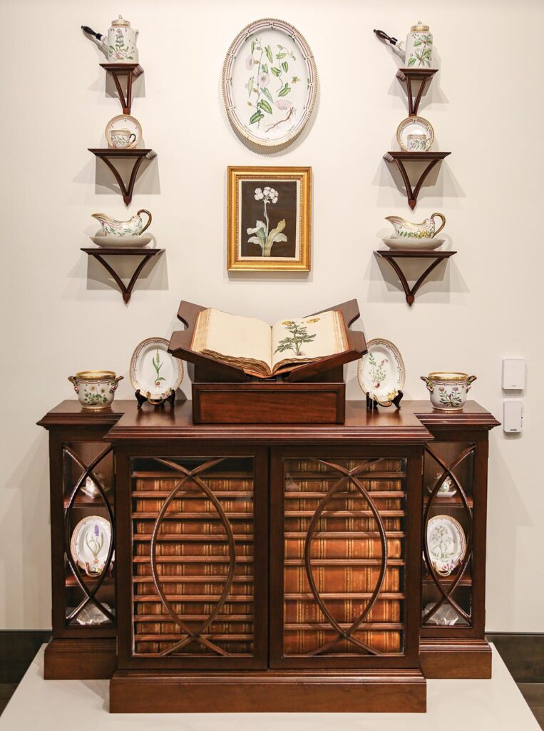 Various Royal Copenhagen Flora Danica porcelains flank the set of the original Flora Danica tomes from which the detailed patterns are taken.