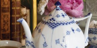 Royal Copenhagen’s Blue Fluted Full Lace teapot, adorned with the soothing and beloved color combination, exudes a delicate elegance due to its intricate lacy details, meticulous craftsmanship, and beautifully feminine shape, juxtaposed with the whimsical faces on the bases of the spout and handle.