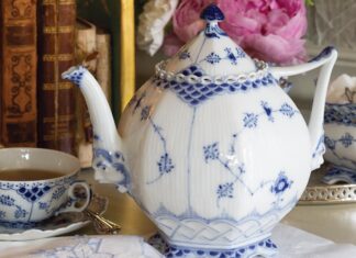 Royal Copenhagen’s Blue Fluted Full Lace teapot, adorned with the soothing and beloved color combination, exudes a delicate elegance due to its intricate lacy details, meticulous craftsmanship, and beautifully feminine shape, juxtaposed with the whimsical faces on the bases of the spout and handle.