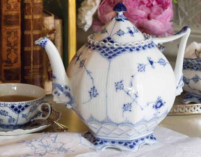 Royal Copenhagen’s Blue Fluted Full Lace teapot, adorned with the soothing and beloved color combination, exudes a delicate elegance due to its intricate lacy details, meticulous craftsmanship, and beautifully feminine shape, juxtaposed with the whimsical faces on the bases of the spout and handle.